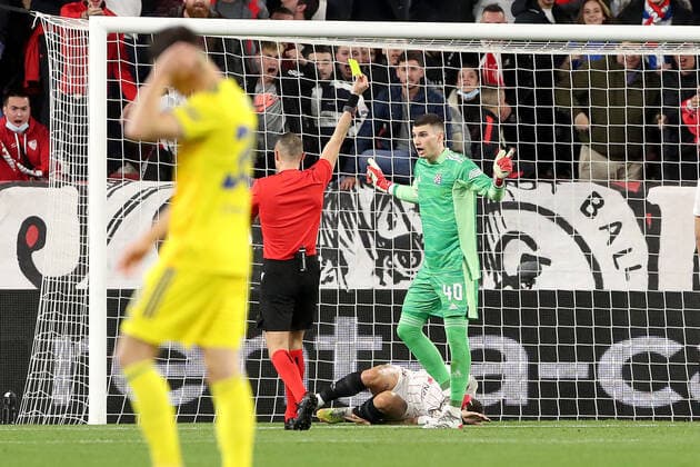 Sevilla FC v Dinamo Zagreb: Knockout Round Play-Offs Leg One - UEFA Europa League Alejandro Gomez of FC Sevilla lies on the pitch injured as Referee Marco Guida show the yellow card for Goalkeeper Dominik Livakovic of Dinamo Zagreb during the UEFA Europa League Knockout Round Play-Offs Leg One match between Sevilla FC and Dinamo Zagreb at Estadio Ramon Sanchez Pizjuan on February 17, 2022 in Seville, Spain. GoranxStanzl PIXSELL