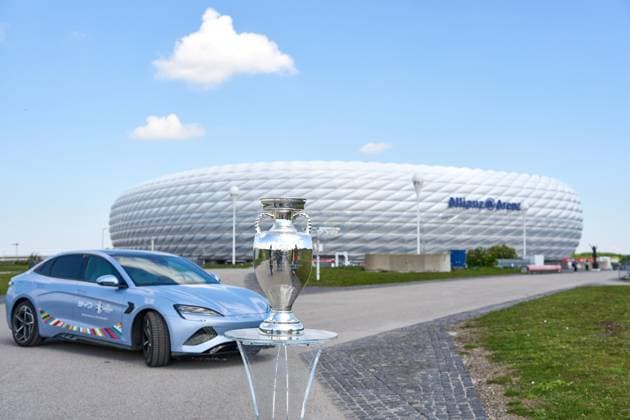 BYD E-Auto mit UEFA Logo vor dem Fußball Stadion der Allianz Arena in München zusammen mit dem Siegerpokal, Henri-Delaunay-Pokal . Offizieller E-Mobilitätspartner der UEFA Euro 2024