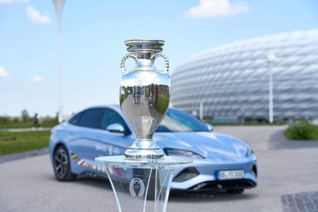 BYD E-Auto mit UEFA Logo vor dem Fußball Stadion der Allianz Arena in München zusammen mit dem Siegerpokal, Henri-Delaunay-Pokal . Offizieller E-Mobilitätspartner der UEFA Euro 2024
