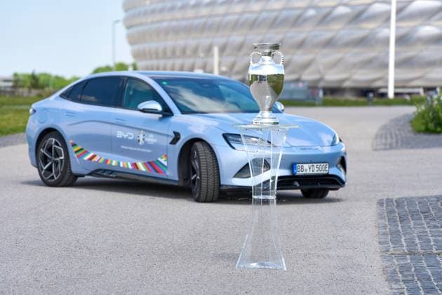BYD E-Auto mit UEFA Logo vor dem Fußball Stadion der Allianz Arena in München zusammen mit dem Siegerpokal, Henri-Delaunay-Pokal . Offizieller E-Mobilitätspartner der UEFA Euro 2024