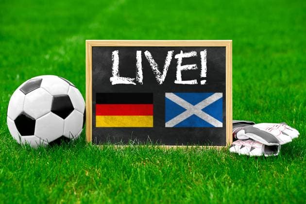 Fußball Europameisterschaft 2024 Themenbild: Live-Übertragung des Spiels Deutschland gegen Schottland Konzept. Ein Fußball mit einer Tafel und Handschuhen auf dem Spielfeld mit Aufschrift: Live! FOTOMONTAGE