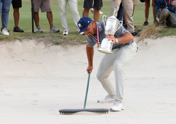 Bryson DeChambeau smooths the sand in a bunker as he celebrates after winning the 124th U.S. Open golf championship at Pinehurst Resort & Country Club in Pinehurst, N.C. on Sunday, June 16, 2024. DeChambeau won with a six-under-par score of 274.  NCP20240616679 JOHNxANGELILLO