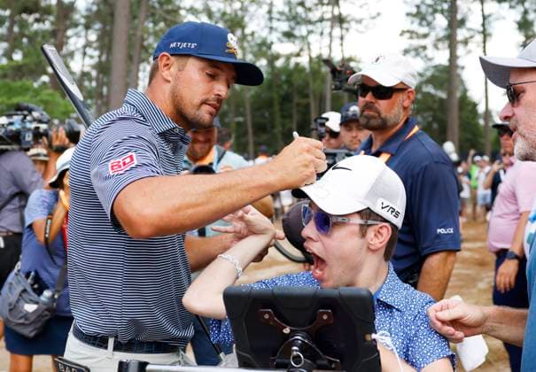 Bryson DeChambeau puts his autograph on the cap of a fan as he walks to the 11th tee box before winning the 124th U.S. Open golf championship at Pinehurst Resort & Country Club in Pinehurst, N.C. on Sunday, June 16, 2024. DeChambeau won with a six-under-par score of 27.  NCP20240616911 JOHNxANGELILLO
