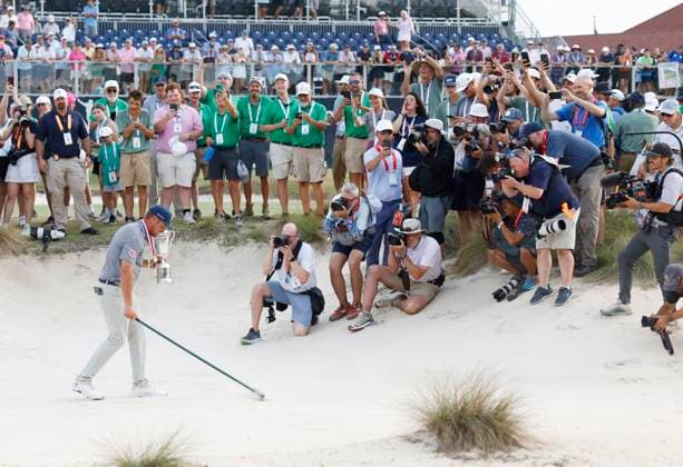Bryson DeChambeau rakes a bunker holding the championship trophy after winning the 124th U.S. Open golf championship at Pinehurst Resort & Country Club in Pinehurst, N.C. on Sunday, June 16, 2024. DeChambeau won with a six-under-par score of 27.  NCP20240616917 JOHNxANGELILLO