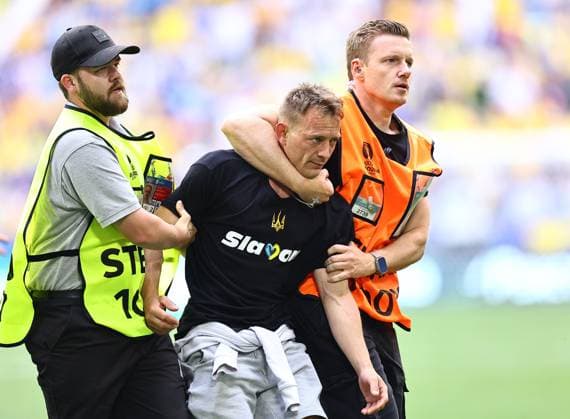A Ukraine fan is escorted from the pitch Romania v Ukraine, UEFA European Championship, EM, Europameisterschaft 2024, Group E, Football, Munich Football Arena, Munich, Germany, 17 Jun 2024 EDITORIAL USE ONLY No use with unauthorised audio, video, data, fixture lists, club league logos or live services. Online in-match use limited to 120 images, no video emulation. No use in betting, games or single club league player publications. Copyright: xMichaelxZemanek Shutterstockx 14539636bi