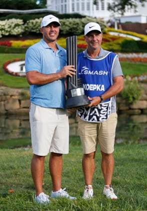 WHITE SULPHUR SPRINGS, WV - AUGUST 18: Smash GC s Captain Brooks Koepka and caddie Ricky Elliott celebrate with the winner s trophy after the final round of the LIV Golf League Greenbrier at The Old White Course on August 18, 2024, in White Sulphur Springs, WV. (Photo by Lee Coleman Icon Sportswire) GOLF: AUG 18 LIV Golf League Greenbrier EDITORIAL USE ONLY Icon155240818101