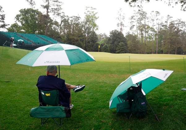 A patron sits under an umbrella waiting to see players on the course before play is suspended due to lightning and thunderstorms in the area during a practice round leading up the Masters Tournament at Augusta National Golf Club in Augusta, Georgia on Monday, April 7, 2025.  AUG20250407125 JOHNxANGELILLO