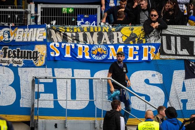 Jena , 270925, Soccer Regionalliga , FC Carl Zeiss Jena vs Chemnitzer FC in the picture Fans Ultras Jena Horda provoke interruption of the game by displacing two escape gates with banners and fans in the block stelv head of the office Flori Zweigler r who is the legal capo of the Ultras