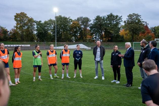 14 10 2025, GER, Visit of the Federal President at a training session of the SG 99 Andernach womens soccer team After the arrival of Federal President Frank Walter Steinmeier, the players interrupt their training session to welcome him The players and staff team stand together in a circle
