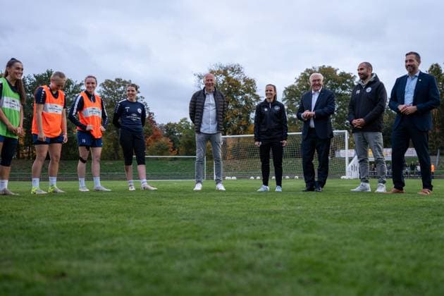 14 10 2025, GER, Visit of the Federal President at a training session of the SG 99 Andernach womens soccer team After the arrival of Federal President Frank Walter Steinmeier, the players interrupt their training session to welcome him The players and staff team stand together in a circle