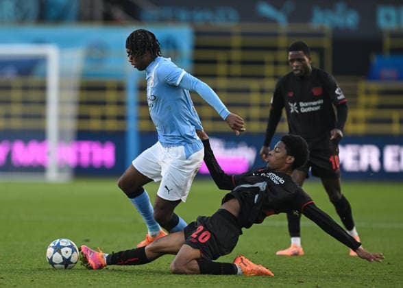 Manchester, England, 25th November 2025. Nebe Sirak Domnic of Bayer Leverkusen tackles Reigan Heskey of Manchester City during the Manchester City U19 vs Bayer Leverkusen U19 UEFA Youth League match at the Academy Stadium, Manchester. Picture credit should read: Cody Froggatt Sportimage EDITORIAL USE ONLY. No use with unauthorised audio, video, data, fixture lists, club league logos or live services. Online in-match use limited to 120 images, no video emulation. No use in betting, games or single club league player publications. SPI_008_CF_MANCHESTER_CITY_U19_V_BAYER_LEVERKUSEN_U19 SPI-4326-0008