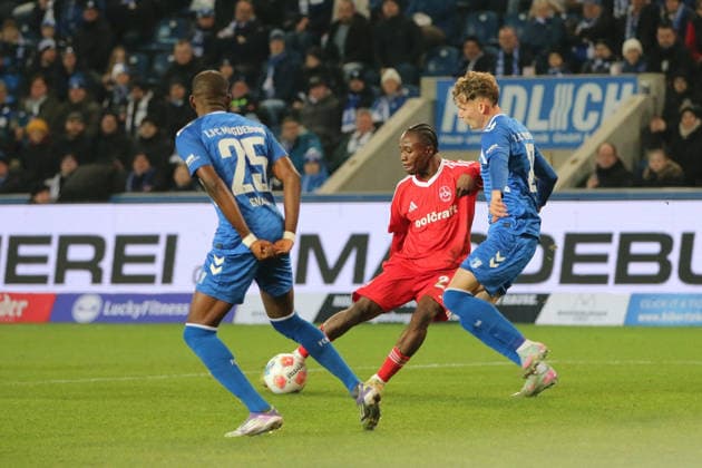 29 11 2025 Soccer Men 2025 2026 2 Bundesliga 14 Matchday 1 FC Magdeburg 1 FC Nürnberg Avnet Arena Magdeburg Mohamed Ali Zoma FCN, red with a shot on goal Philipp Hercher FCM, blue, right still tries to block Silas Gnaka FCM, blue, 25 awaits the shot Magdeburg Saxony Anhalt Germany