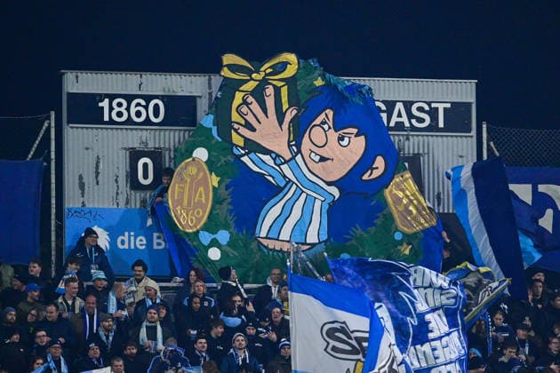 The fans of TSV 1860 Muenchen have hung a Pumukel with blue hair and a blue and white jersey in front of the scoreboard, 20 12 2025, Munich Germany , Football, 3 Liga, TSV 1860 München SC Verl, DFB DFL REGULATIONS PROHIBIT ANY USE OF PHOTOGRAPHS AS IMAGE SEQUENCES AND OR QUASI VIDEO xslx