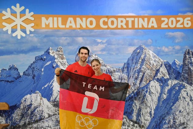 Minerva Fabienne Hase und Nikita Volodin (GER), Eiskunstlauf,Paarlauf.Paarlaeufer vor Alpenkulisse, Dolomiten und Team D Flagge,Fahne, schwarz rot gold. Einkleidung Team Deutschland fuer die Winterspiele 2026 in Mailand und Cortina am 19.01.2026,
