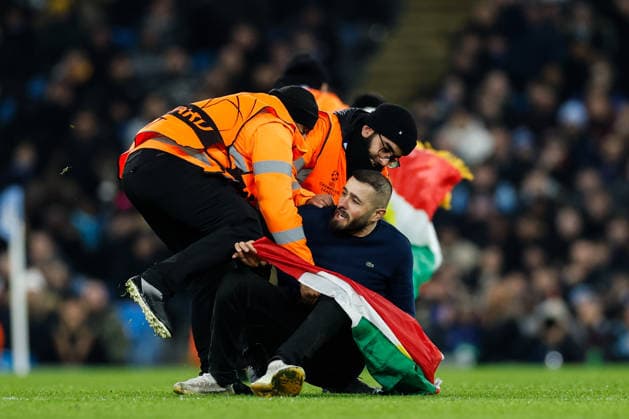 Manchester, England, 28th January 2026. Pitch invaders are removed as they hold up the Kurdistan flag during the Manchester City vs Galatasaray UEFA Champions League match at the Etihad Stadium, Manchester. Picture credit should read: Andrew Yates Sportimage EDITORIAL USE ONLY. No use with unauthorised audio, video, data, fixture lists, club league logos or live services. Online in-match use limited to 120 images, no video emulation. No use in betting, games or single club league player publications. SPI_041_CF_Man_City_Galatasaray SPI-4489-0098