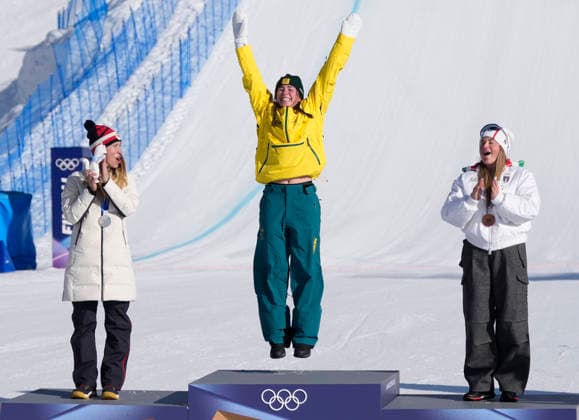 Gold medalist Josie Baff of Australia (C) jumps as she is introduced with silver medalist Eva Adamczykova of Czechia (L) and bronze medalist Michela Moioli of Italy on the podium after the Women s Snowboard Cross finals at the Milano Cortina 2026 Winter Olympic Games, Olympische Spiele, Olympia, OS in Livigno, Italy, on Friday, February 13, 2026.  OLY20260213806 BOBxSTRONG