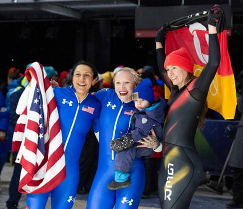 February 16, 2026, Cortina D ampezzo, Lombardy, Italy: From left, Golf medal winner Elana Meyers Taylor of the USA, teammate and bronze medal winner Kaillie Armbruster Humphries holding her son Aulden, and silver medalist Laura Nolte of Germany after the Women s Monobob at the Cortina Sliding Centre for the Milano Cortina 2026 Winter Olympics. Cortina Sliding Centre - Monnobob  - ZUMAsc5_ 20260216_oly_sc5_015 Copyright: xErichxSchlegelx