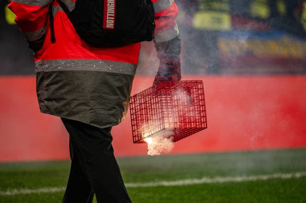 26th February 2026; The City Ground, Nottingham, England; UEFA Europa League Football, Nottingham Forest versus Fenerbahce; A fire marshal collects flares thrown by Fenerbahce SK fans  GodfreyxPitt Content restricted for UK based newspaper