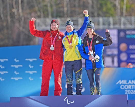 (260308) -- TESERO, March 8, 2026 -- Gold medalist Oleksandra Kononova (C) of Ukraine celebrates on the podium alongside silver medalist Natalie Wilkie (L) of Canada and bronze medalist Liudmyla Liashenko of Ukraine during the awarding ceremony for the para biathlon women s sprint standing at the Milan-Cortina 2026 Paralympic Winter games, Winterspiele,Spiele, Summer games in Tesero, Italy, March 7, 2026. ) (SP)ITALY-TESERO-PARALYMPIC WINTER GAMES-PARA BIATHLON-WOMEN S SPRINT STANDING HouxZhaokang 
