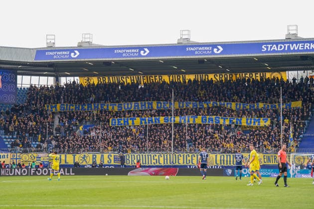 Germany Soccer 2 Bundesliga 2025 2026, 29 Matchday VfL Bochum vs Eintracht Braunschweig Vonovia Ruhrstadion Bochum, Germany, Europe, Guest block, Fans, Spectators, Crowd, Fan curve, Away fans, Choreography, Banner, Banner In the security mania lost the mind is how you deal with guests , protest, criticism, fan culture, mood, atmosphere, tribune, long shot, interior view, sports stadium, club colors yellow blue, fence flags, flags, support, competition, professional league, match scene, players in foreground, referee, pitch, turf Copyright: xJOERANxSTEINSIEKx