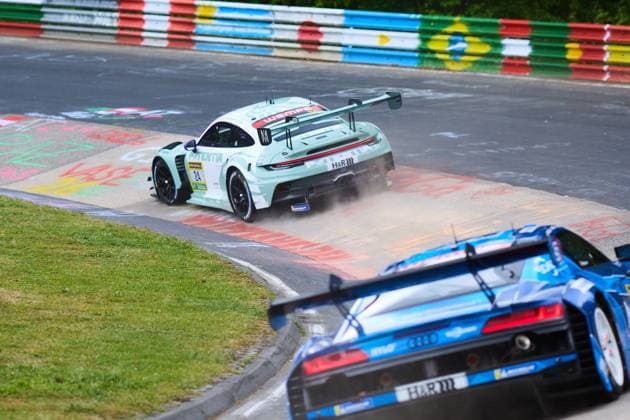 The mint-colored Porsche 911 GT3 with the starting number 24 from Lionspeed GP hits the curb while negotiating a bend on the Nürburgring and stirs up dust The sponsors H R and Wempe are clearly visible on the bodywork In the foreground, the rear of a blue Audi can also be seen on the Nordschleife Laurens Vanthoor Laurin Heinrich Ricardo Feller Lionspeed GP Porsche 911 GT3 24 from Lionspeed GP in the bend at the Nürburgring Copyright: xspeedshotx