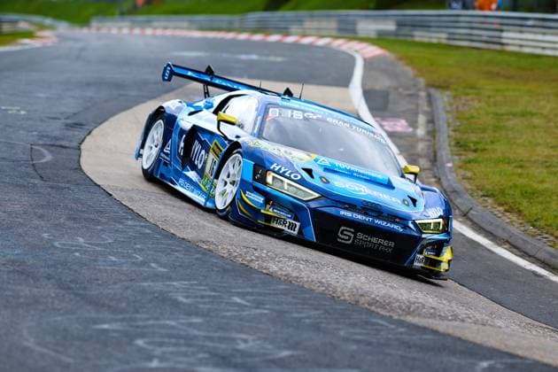 The Audi R8 LMS GT3 with starting number 16 from Scherer Sport PHX drives through a corner on the Nordschleife of the Nürburgring The blue car Alexander Sims Ben Green Christopher Haase Scherer Sport PHX bears the sponsors HYLO, IRS Dent Wizard and TÜV Rheinland prominently on the bodywork The white rims with Michelin tires and the striking rear wing underline the GT3 character of the Audi R8 LMS GT3 16 from Scherer Sport PHX on the corner Copyright: xspeedshotx