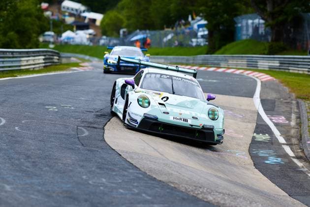 The Porsche 911 GT3 R Lukas Ertl Matthias Benndorf Maximilian Johannes Ertl Stefan Ertl Reiter Engineering from Reiter Engineering drives through a tight bend on the Nordschleife of the Nürburgring The mint green vehicle with the striking purple accents and the Gran Turismo sponsoring clearly bears the starting number 91 as well as the H R and Michelin lettering In the background, another GT3 vehicle in blue livery follows Porsche 911 GT3 R 91 from Reiter Engineering in the Nordschleife bend Copyright: xspeedshotx