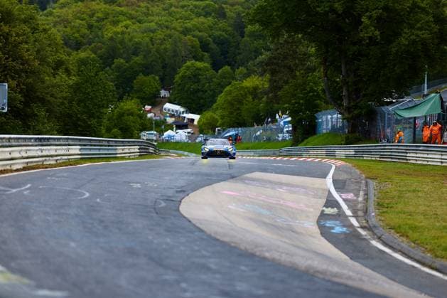 A blue Mercedes AMG GT3 with the starting number 99 drives through a characteristic bend on the Nordschleife of the Nürburgring The typical green hills of the Eifel can be seen in the background as well as track marshals in orange equipment The red and white curbs and the curved track layout emphasize the special character of this legendary race track Mercedes AMG GT3 99 on the Nordschleife at the Nürburgring Copyright: xspeedshotx