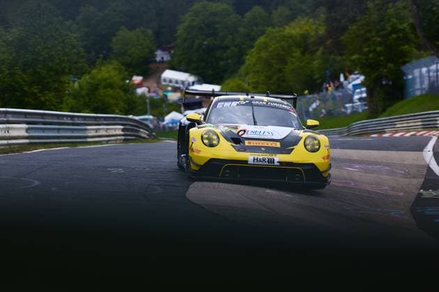 The yellow and black Porsche 911 GT3 Bastian Buss Michael Christensen Michael Klitgaard Christensen Dinamic GT from Dinamic GT drives through a curve on the Nordschleife of the Nürburgring The vehicle bears the sponsors H R, Pirelli and Endless and is branded with Gran Turismo In the background you can see the typical green hills of the Eifel as well as spectators at the edge of the track Porsche 911 GT3 from Dinamic GT on the Nordschleife Copyright: xspeedshotx