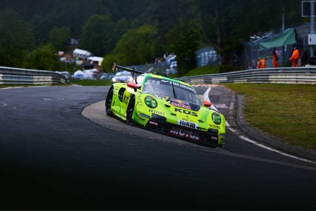 The eye-catching neon yellow Porsche 911 GT3 R with the starting number 911 from Manthey negotiates a tight bend on the Nordschleife of the Nürburgring The car Ayhancan Güven Kevin Estre Thomas Preining Manthey prominently bears the sponsors KÜS, Veltins, Motul, Red Bull and H R and stands out with its striking neon yellow and black color design Track marshals and spectator areas can be seen in the background Manthey Porsche 911 GT3 R 911 takes a bend on the Nordschleife Copyright: xspeedshotx