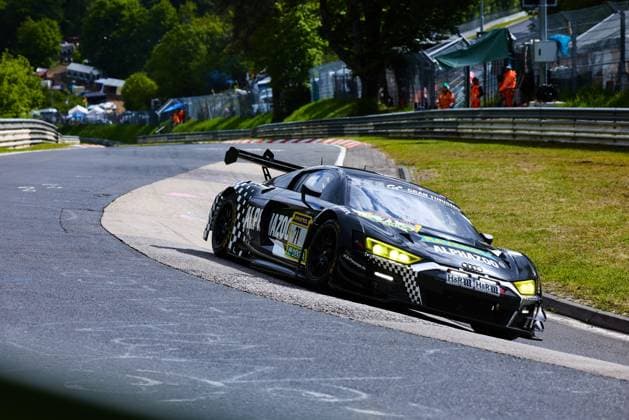The Audi R8 LMS GT3 with starting number 71 from JUTA Racing negotiates a tight bend on the Nordschleife of the Nürburgring The black and white checkered car with the sponsors Alphazoo and RAVENOL is on the road with bright yellow headlights In the background, track marshals in orange clothing and spectator areas can be seen Björn Großmann Christer Jöns Otto Blank Pierre Kaffer JUTA Racing Audi R8 LMS GT3 71 from JUTA Racing on the Nordschleife Copyright: xspeedshotx