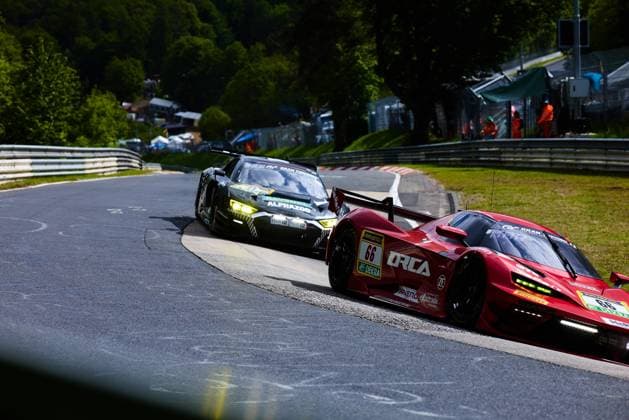 The red car with starting number 66 from Reiter Engineering drives through a tight bend on the Nordschleife at the Nürburgring The sponsors ORCA, RAVENOL, ZF and exprotrade are clearly recognizable on the hood and flanks, black and green GT3 vehicle with RAVENOL and ALPHAZOO sponsorship In the background, track marshals in orange clothing and the typical green Eifel scenery can be seen Arne Hoffmeister Julien Apotheloz Laurents Hörr Marcel Marchewicz Miklas Born Reiter Engineering Reiter Engineering 66 and dark GT3 vehicle on the Nordschleife Copyright: xspeedshotx