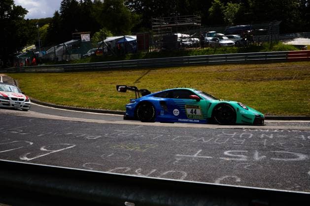 The Porsche 911 GT3 R Klaus Bachler Morris Schuring Sven Müller Tim Heinemann Falken Motorsports from Falken Motorsports drives through a corner on the Nordschleife of the Nürburgring The vehicle bears the characteristic blue and turquoise Falken design with the sponsors RAVENOL, DEKRA and Falkentyre com Another vehicle with H R sponsorship can be seen in the background Falken Motorsports Porsche 44 on the Nordschleife Copyright: xspeedshotx