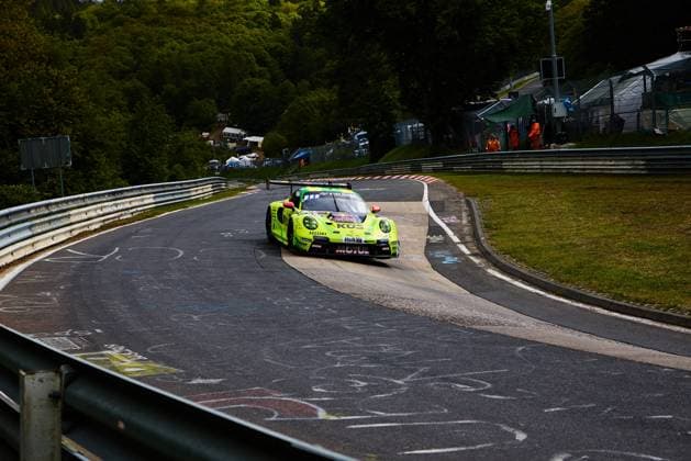 The striking yellow-green Porsche 911 GT3 with starting number 911 from Manthey negotiates a tight bend on the Nordschleife of the Nürburgring at the ADAC RAVENOL 24h Nürburgring 2026 The car sponsored by Red Bull, KÜS and Veltins Ayhancan Güven Kevin Estre Thomas Preining Manthey takes the bend precisely, while marshals in orange equipment can be seen in the background Porsche 911 GT3 911 from Manthey on the Nordschleife Copyright: xspeedshotx