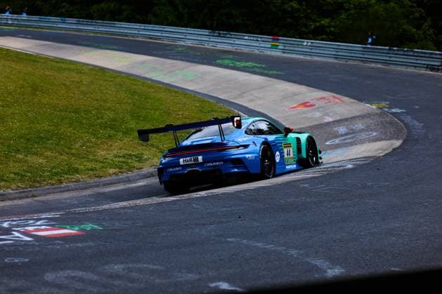 The Porsche 911 GT3 with the starting number 44 from Falken Motorsports drives through a curve on the Nordschleife at the Nürburgring The car Klaus Bachler Morris Schuring Sven Müller Tim Heinemann Falken Motorsports wears the characteristic blue and green Falken livery with the sponsors H R and RAVENOL and is equipped with a striking rear wing The typical colorful chalk pictures on the asphalt of the Nordschleife can be seen in the foreground Falken Motorsports Porsche 911 GT3 44 on the Nordschleife Copyright: xspeedshotx