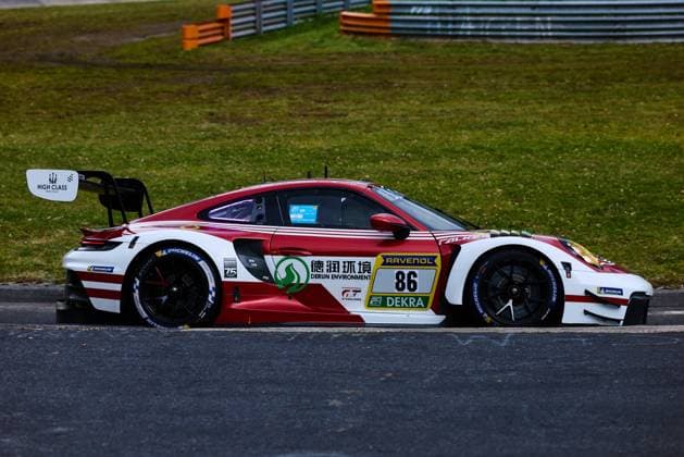 The Porsche 911 GT3 with starting number 86 from High Class Racing drives through a bend on the Nürburgring The red and white vehicle Anders Fjordbach Hongli Ye Kerong Li King Harry High Class Racing bears the sponsors Derun Environment, RAVENOL and DEKRA prominently on the body Michelin tires and the characteristic rear wing setup of the GT3 racing car are clearly visible Porsche 911 GT3 86 from High Class Racing on the Nürburgring Copyright: xspeedshotx