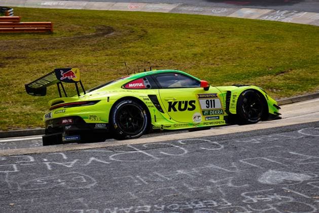 The neon yellow Porsche 911 GT3 R with the starting number 911 of the Manthey team drives through a bend on the Nürburgring The strikingly designed vehicle Ayhancan Güven Kevin Estre Thomas Preining Manthey bears the sponsors KÜS, RAVENOL, Motul, Red Bull and Michelin prominently on the bodywork The large rear wing with Red Bull branding and the aerodynamic add-on parts emphasize the racing character of the GT3 vehicle Porsche 911 GT3 R 911 by Manthey in neon yellow at the Nürburgring Copyright: xspeedshotx