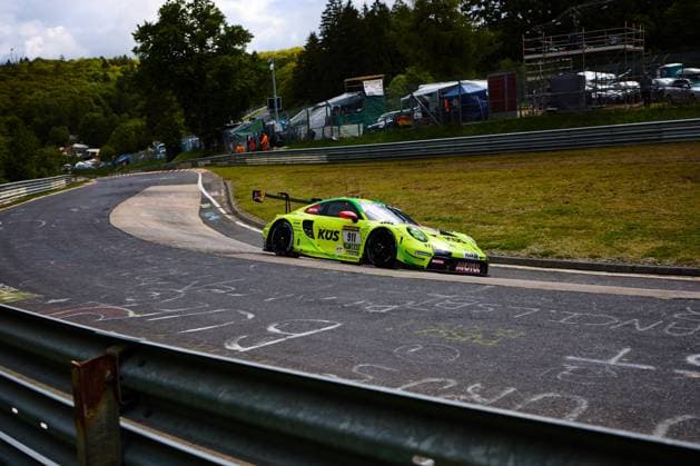 The striking neon yellow green Porsche 911 GT3 R with starting number 911 from Manthey takes a tight right-hand bend on the Nürburgrings Nordschleife The car Ayhancan Güven Kevin Estre Thomas Preining Manthey with sponsors KÜS, MOTUL and RAVENOL drives through the characteristic bend, while the wooded Eifel hills and the paddock are visible in the background Porsche 911 GT3 R 911 from Manthey on the Nordschleife Copyright: xspeedshotx