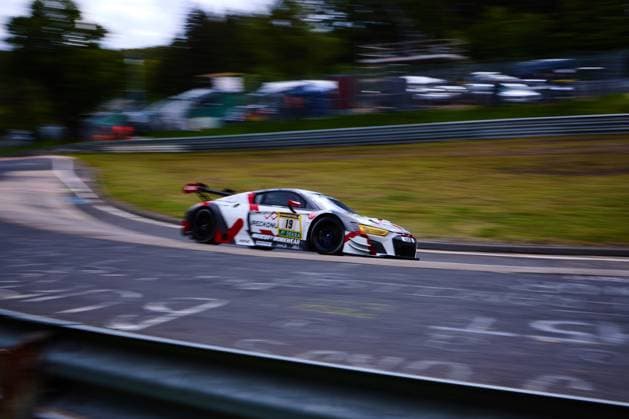 A white Audi R8 LMS with starting number 19 dynamically drives through a bend at the Nürburgring The car has a striking red and white design with the sponsors PECKIONI and MOODY S WORKWEAR as well as the DEKRA logo The panning shot emphasizes the high speed of the GT car at the 24-hour race on the Nordschleife Audi R8 LMS 19 with panning shot at the Nürburgring Copyright: xspeedshotx