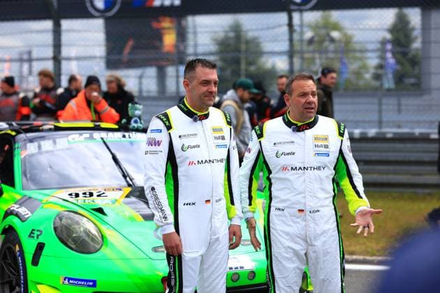 Two drivers of the Manthey Team eFuel Griesemann stand in white racing overalls with green and yellow accents in front of the characteristic green Porsche 911 GT3 with the starting number 992 Sponsors such as Manthey, H R, RAVENOL, Griesemann and eFuels are clearly visible In the background is the paddock of the Nürburgring with marshals and other spectators The picture was taken during the ADAC RAVENOL 24h Nürburgring 2026 Björn Griesemann Dirk Adorf Georg Griesemann Marco Holzer Manthey Team eFuel Griesemann Manthey 992 drivers in front of the Porsche 911 GT3 at the Nürburgring Copyright: xspeedshotx