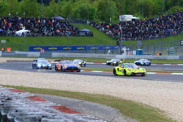 The yellow-green Porsche 911 GT3 R with the starting number 911 from Manthey leads the field through a bend on the Nürburgring Closely behind it follows a Mercedes AMG GT3 with Red Bull livery and a blue Audi R8 LMS GT3 In the background, other GT3 cars fight for positions while thousands of spectators watch the spectacular race from the grandstands and the trackside The Goodyear advertising banners line the track Lukas Ertl Matthias Benndorf Maximilian Johannes Ertl Stefan Ertl Reiter Engineering Porsche 911 leads GT3 field at the 24h Nürburgring Copyright: xspeedshotx