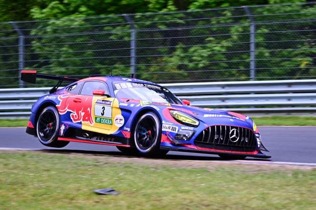 The Mercedes AMG GT3 with the starting number 3 of the Mercedes AMG Team Verstappen Racing drives through a curve on the Nürburgring The vehicle Daniel Juncadella Jules Gounon Lucas Auer Max Verstappen Mercedes AMG Team Verstappen Racing wears a striking Red Bull livery in blue, red and yellow and features sponsors such as RAVENOL, DEKRA and H R The photo shows the vehicle driving fast on the Nordschleife, surrounded by green vegetation and crash barriers Mercedes AMG GT3 3 by Verstappen Racing on the Nordschleife Copyright: xMichaelxGelhardtx
