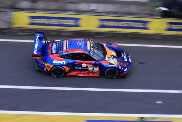 The Porsche 911 GT3 R with starting number 4 from Goroyan RT by Car Collection crosses the pit lane at the Nürburgring The vehicle Alex Fontana Artur Goroyan Nathanael Berthon Oleg Kivtka Oleg Kvitka Goroyan RT by Car Collection wears a striking blue orange red color scheme with the sponsors GRT, GInvest, RAVENOL and Falken The characteristic Castrol advertising banner is visible in the background Porsche 911 GT3 R 4 from Goroyan RT by Car Collection at the Nürburgring Copyright: xspeedshotx