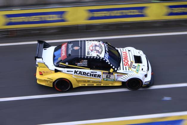 The car Luca Ludwig Markus Winkelhock Sebastian Asch HWA Engineering Speed from HWA Engineering Speed drives through the Nürburgring pit lane at high speed The striking yellow and white Kärcher livery with Sonax and Falken sponsorship is clearly recognizable The car bears the starting number 62 and the driver line-up of Asch, Ludwig, Winkelhock and Adelson is listed on the drivers door HWA Engineering Speed 62 with Kärcher livery at the Nürburgring Copyright: xspeedshotx