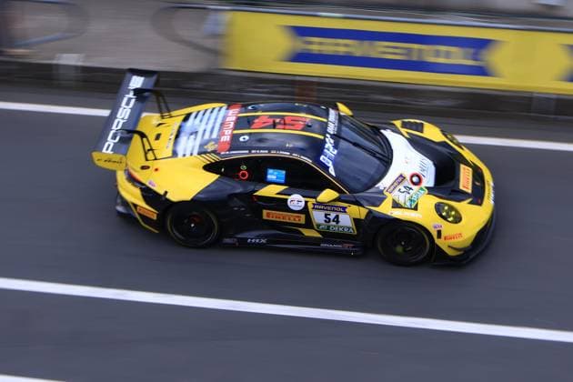 The Porsche 911 GT3 R with the starting number 54 of the Dinamic GT team drives through the pit lane at the Nürburgring The vehicle presents itself in the striking black and yellow design with sponsors such as Ravenol, Pirelli and Wempe Bastian Buss Michael Christensen Michael Klitgaard Christensen Dinamic GT Porsche 911 GT3 R 54 from Dinamic GT in the pit lane Copyright: xspeedshotx