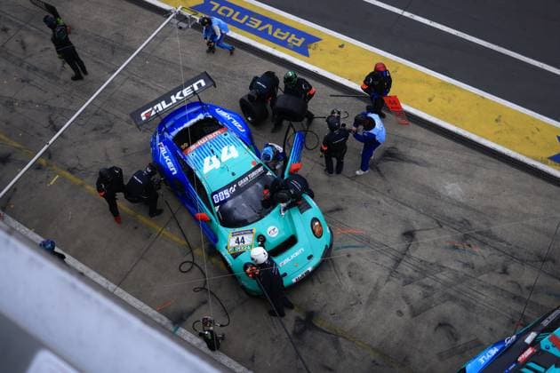 The Falken Motorsports Porsche 911 GT3 R with starting number 44 is parked in the pit lane of the Nürburgring during a pit stop From an elevated birds eye view, the turquoise and blue car of Klaus Bachler Morris Schuring Sven Müller Tim Heinemann Falken Motorsports can be seen, while several mechanics in Falken team clothing work on the car at the same time Sponsor logos of Falken, Gran Turismo and RAVENOL are clearly visible The yellow pit markings with the RAVENOL lettering can be seen in the background Falken Motorsports 44 at the pit stop at the Nürburgring Copyright: xspeedshotx