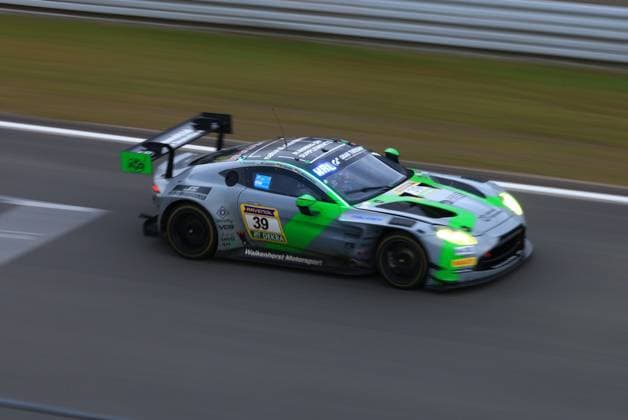 The Henry Walkenhorst Anders Buchardt Mex Jansen Nico Hantke Walkenhorst Motorsport from Walkenhorst Motorsport is on the Nürburgring racetrack at high speed The vehicle in its characteristic gray-green livery with bright green accents shows motion blur, The switched-on headlights indicate twilight or night conditions Sponsors such as RAVENOL and DEKRA are clearly visible on the side of the vehicle Aston Martin Vantage GT3 39 by Walkenhorst Motorsport on the Nürburgring Copyright: xspeedshotx
