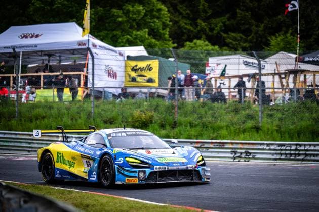 The McLaren GT3 Ben Doerr Marvin Kirchhöfer Timo Glock Timo Scheider Doerr Motorsport from Doerr Motorsport drives through a tight right-hand bend on the Nürburgring Nordschleife The car wears the eye-catching blue and yellow livery with the Bitburger sponsorship and the starting number 69 In the background, spectators and the teams tents are visible, including a KW Suspensions banner and the Grello logo McLaren 69 from Doerr Motorsport in the bend at the Nürburgring Copyright: xMichaelxGelhardtx