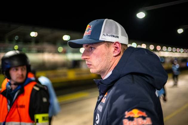 Max Verstappen 3 Driver stands concentrated in the paddock of the Nürburgring He wears a Red Bull AlphaTauri cap and a dark blue Red Bull jacket with Sog and other sponsor logos A marshal in an orange safety vest can be seen in the background, the illuminated pit lane and grandstand lights can be seen blurred in the background Max Verstappen in the paddock at the Nürburgring at night Copyright: xMichaelxGelhardtx