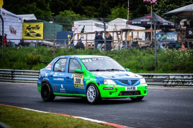 The Dacia Logan Christian Geilfus JS Competition from JS Competition completes a lap on the Nürburgring at the ADAC RAVENOL 24h Nürburgring 2026 The vehicle, painted in striking blue and neon green, bears the starting number 300 and is marked with sponsors such as RAVENOL, Falken, GoodYear, H R and Bleker Autoteile The typical spectator areas of the Nordschleife with fan zones and banners can be seen in the background Dacia Logan 300 from JS Competition on the Nürburgring Copyright: xMichaelxGelhardtx